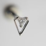 Close-up of a triangular-cut diamond held in a V-shaped silver prong setting on a pale background.