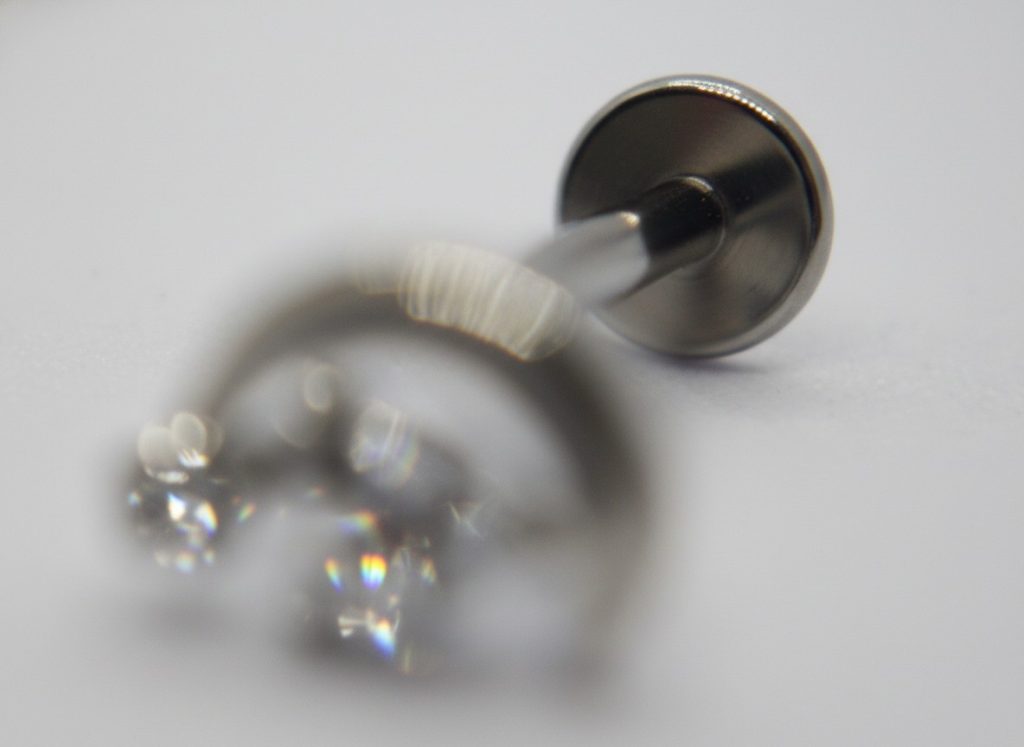 Close-up of a metal stud earring with a faceted clear gemstone blurred in the foreground and the post and backing in focus.