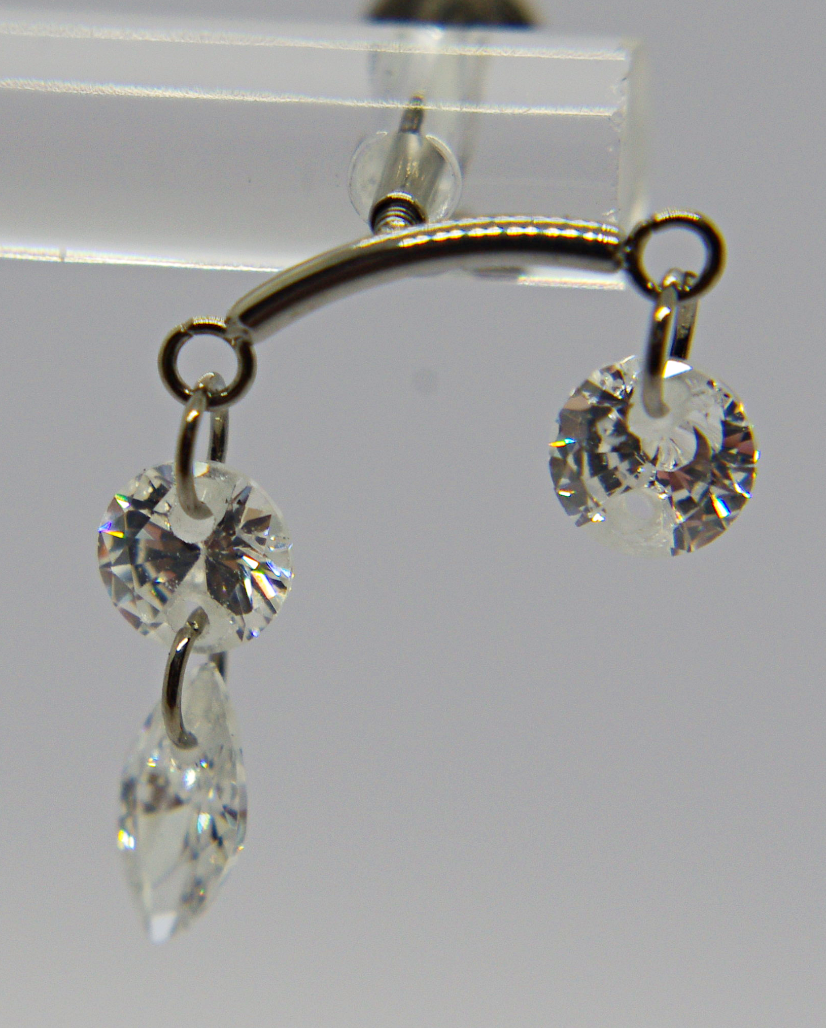 Dangling silver earring with a curved bar holding two clear faceted crystals: a round stone and a teardrop crystal.