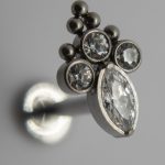 Close-up of a silver stud earring with three small round crystals and a larger marquise-cut crystal in a clustered setting.