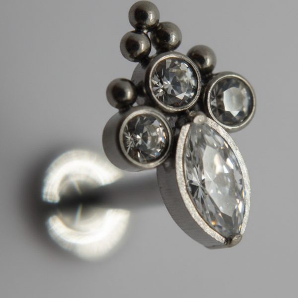 Close-up of a silver stud earring with three small round crystals and a larger marquise-cut crystal in a clustered setting.
