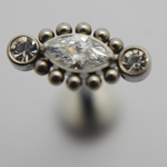 Metal stud featuring a marquise-cut clear gemstone center, two round clear stones at ends, and small metal bead accents.