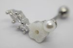 Silver barbell piercing with a white carved flower, small pearl bead and clear prong-set crystals on a blurred white background.