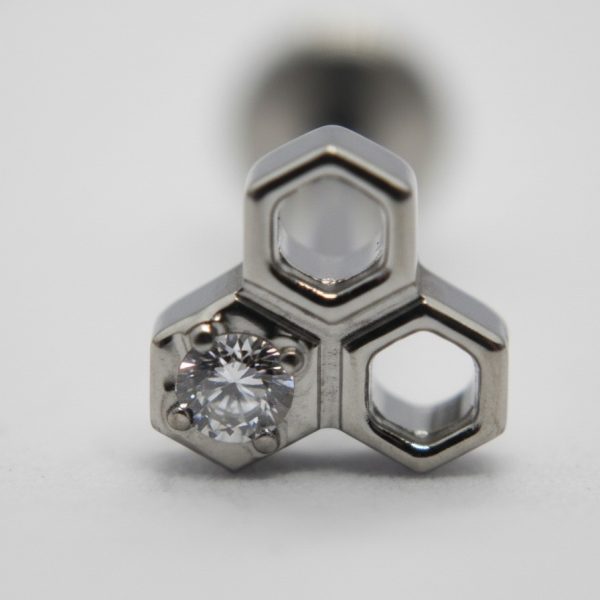 Triangular stainless steel jewelry stud with three hexagonal openings, one set with a round faceted clear gemstone.