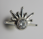 Close-up of a silver sunburst stud with a bezel-set round clear faceted gem and radiating tapered prongs.