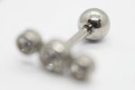 Small silver barbell earring with a round ball on one end and three blurred rhinestone studs on the other, on a white background.