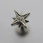 Silver three-dimensional star-shaped stud with a small central gemstone on a soft gray background.