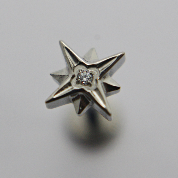 Silver three-dimensional star-shaped stud with a small central gemstone on a soft gray background.