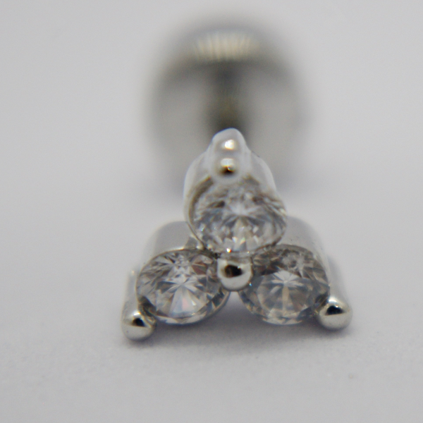 Close-up of a silver stud earring with three round clear stones set in a triangular cluster, screwback post blurred behind.