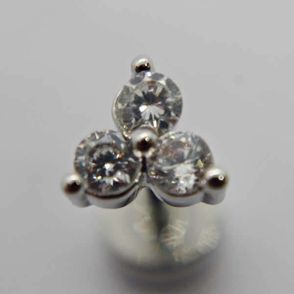 Macro close-up of a silver stud earring with three round clear gemstones arranged in a triangular cluster.