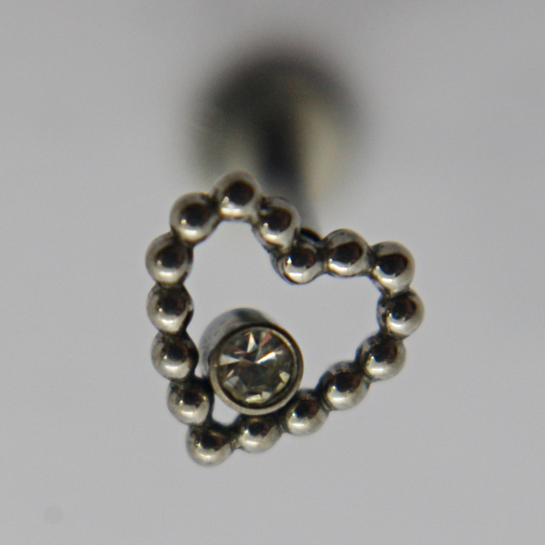 Silver beaded heart-shaped jewelry charm with a small round clear gemstone set near its center on a pale background.