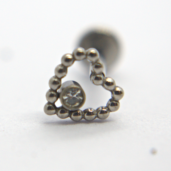 Small beaded silver heart stud with a bezel-set clear gemstone at its center on a white background.