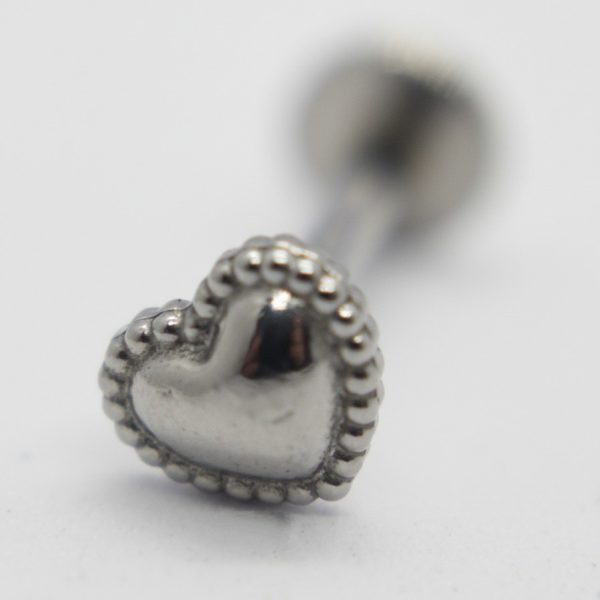 Small silver heart-shaped stud with beaded edge on a white surface, close-up shallow focus.