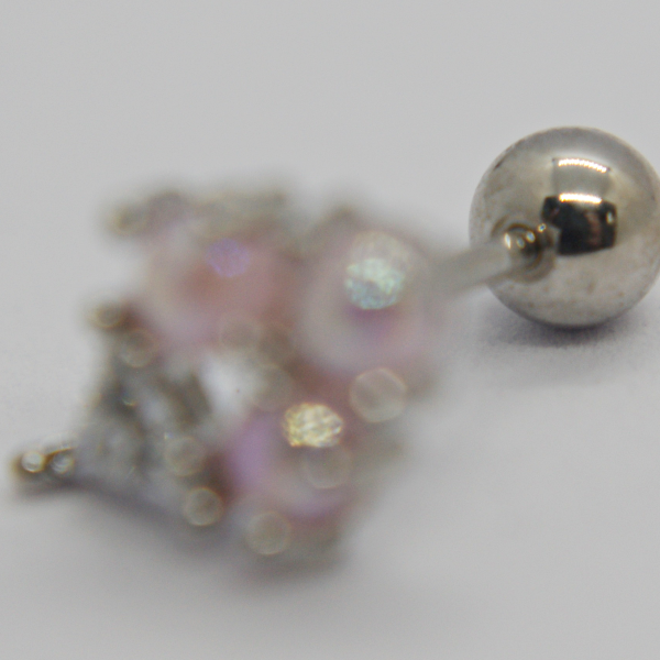 Silver ball-back stud earring in sharp focus with a blurred pink rhinestone ornament lying on a white surface.