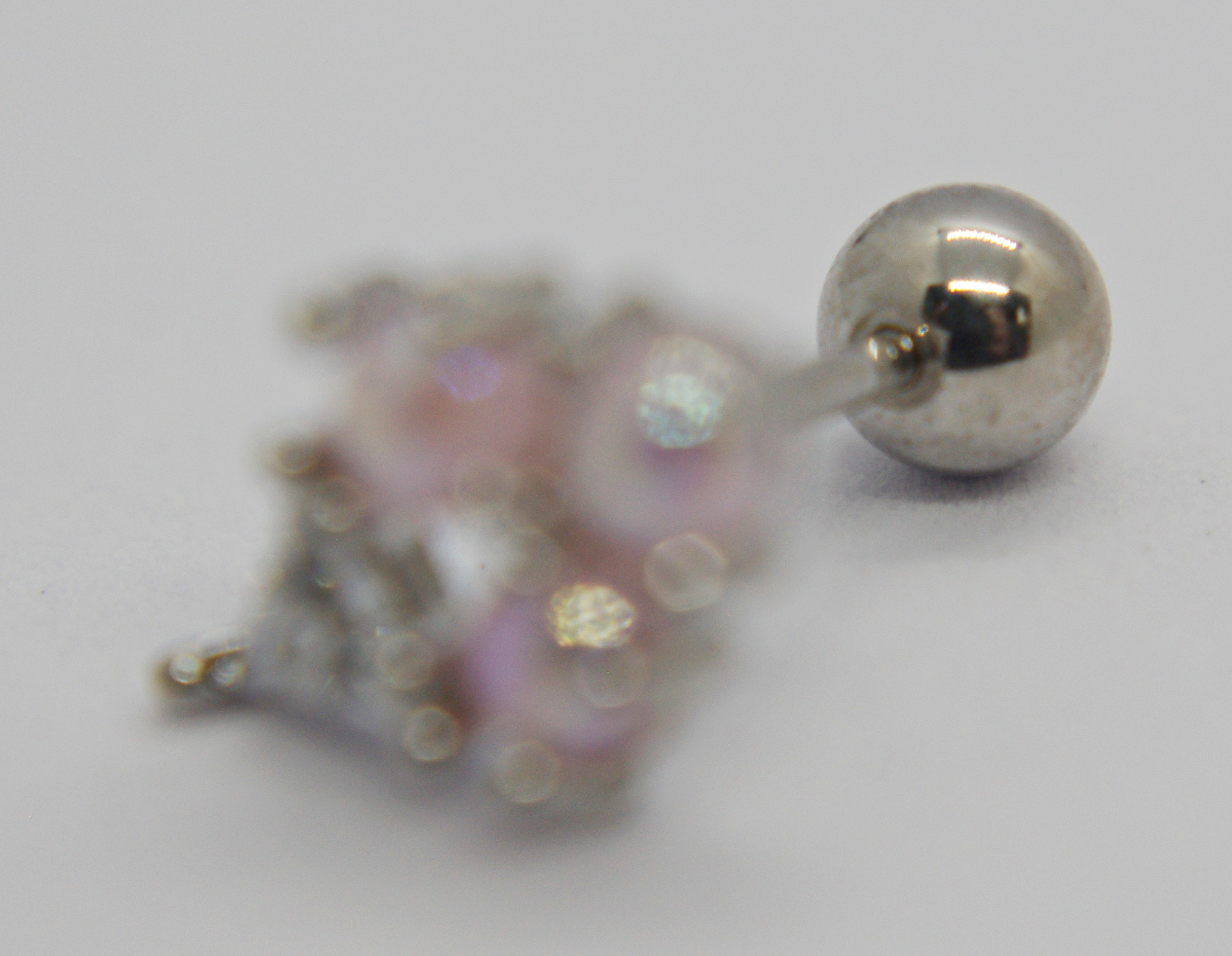 Silver ball-back stud earring in sharp focus with a blurred pink rhinestone ornament lying on a white surface.