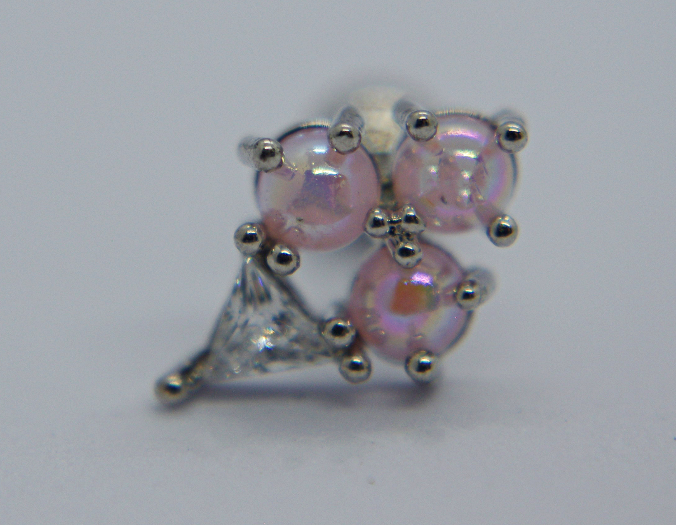 Small silver earring stud with three iridescent pink beads held by prongs and a small triangular clear gem on a pale background.