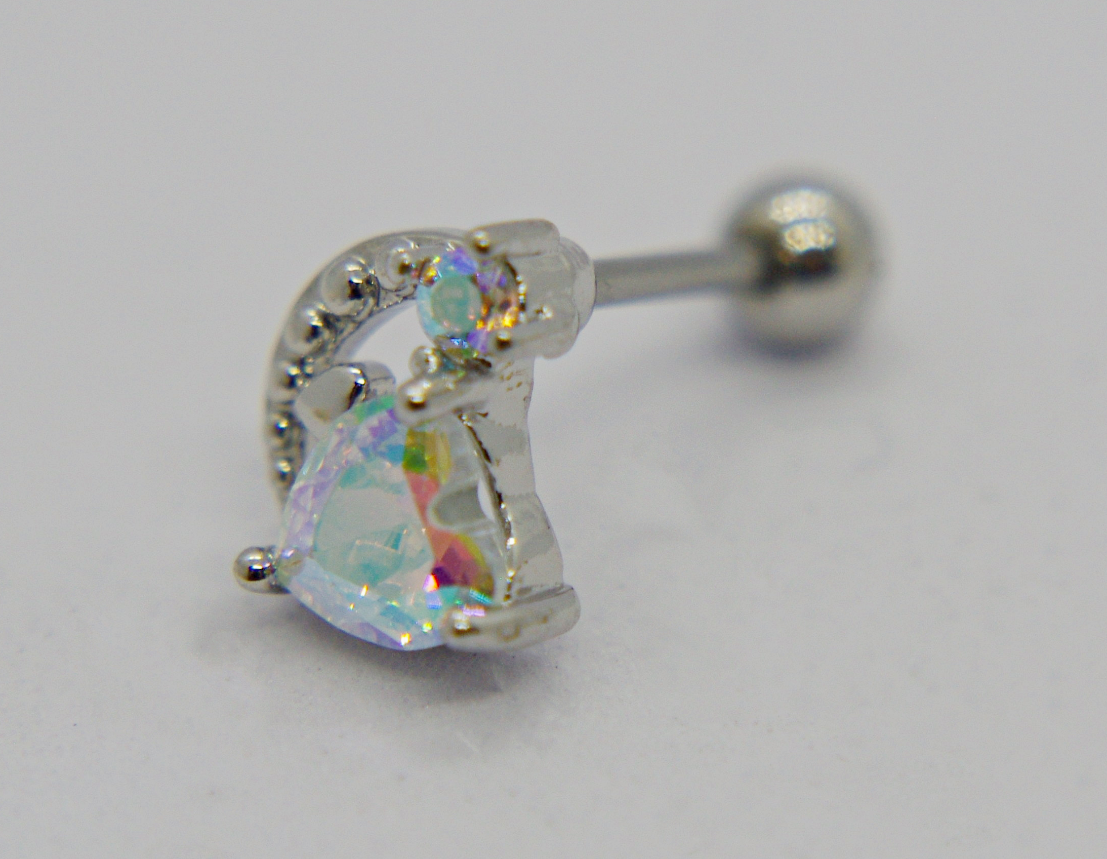 Silver barbell piercing with a heart-shaped iridescent gem set in a decorative crescent stud.