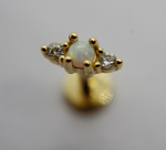 Gold stud earring with a central opal cabochon held by prongs, flanked by two small round clear stones on a pale background
