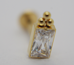 Macro view of a gold stud earring with a rectangular faceted clear stone set in a bezel and three small gold beads above.