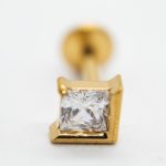 Close-up of a gold stud earring with a square-cut clear gemstone in a four-prong setting and visible post.