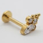 Gold labret stud with a bezel-set large oval gemstone, three smaller round stones, and three tiny gold beads.