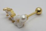 Gold barbell earring with three clear stones and a small carved white flower topped by a pearl on a white surface.