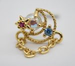 Gold-tone charm with a star holding a pink gem, an iridescent center stone, a blue gem, beaded crescent and short chain.