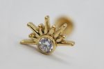 Gold sunburst stud earring with a round clear gemstone in the center on a white background.