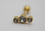 Gold stud with three bezel-set clear gems, a larger center stone flanked by two smaller stones on a white surface.
