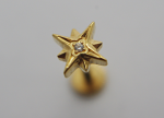 Close-up of a gold star-shaped stud earring with a small clear gemstone set in its center against a neutral background