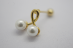 Gold earring stud with two white pearls joined by a small curved gold loop, lying on a soft white background.