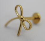 Close-up of a small polished gold bow-shaped earring stud with its push-back resting on a white surface.