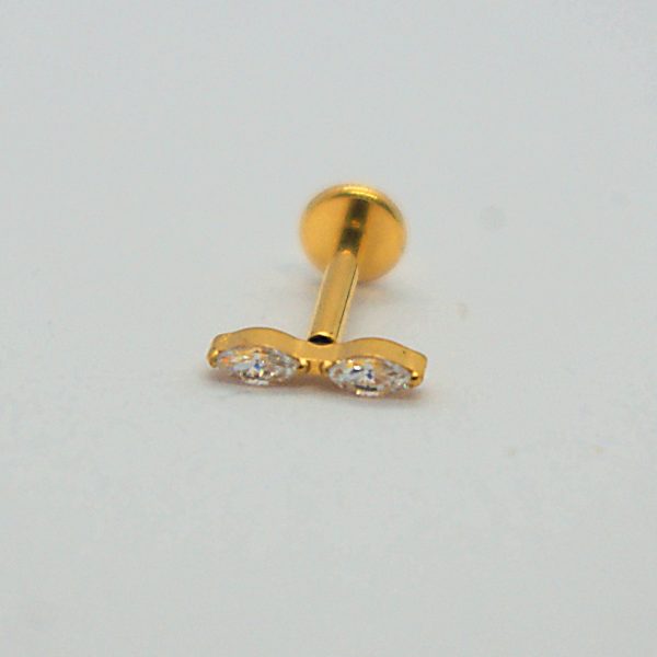 Gold labret earring stud with two marquise-shaped clear stones set side-by-side, lying on a plain white surface.