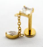 Gold labret-style stud with a short chain and faceted clear gemstone charm resting on a white surface