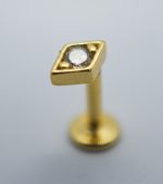 Gold labret stud with a rhombus-shaped top holding a small clear round gem, photographed close-up on a gray background.