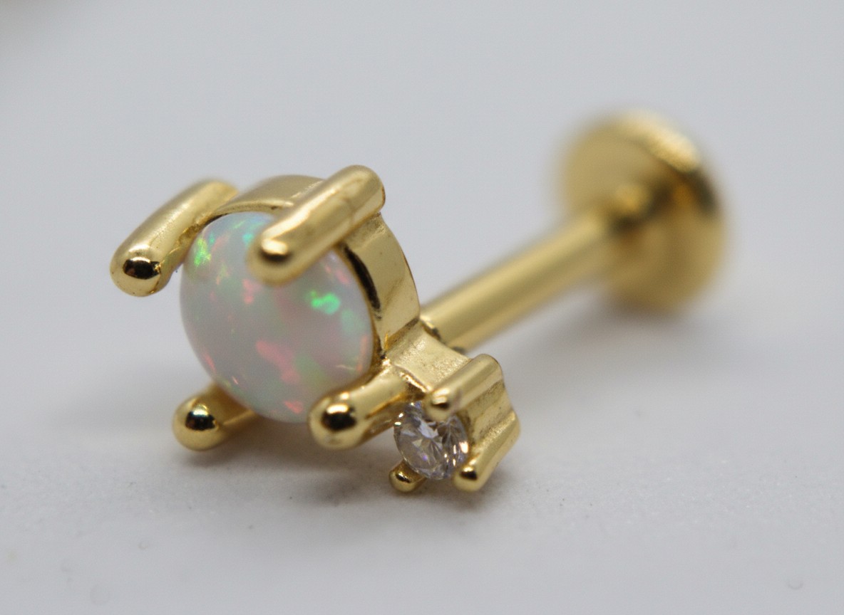 Gold stud earring with round opal cabochon in four-prong setting and small clear accent stone.