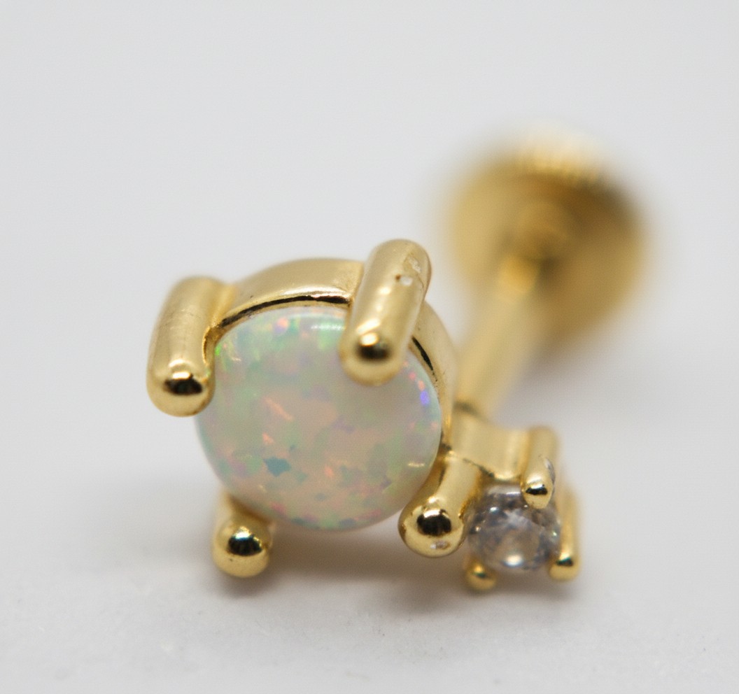 Close-up gold stud earring with round opal showing multicolored play-of-color beside a small clear gemstone in prong setting