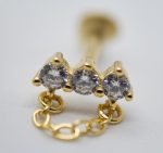 Close-up of a gold stud earring with three prong-set round clear gemstones and a short linked gold chain.