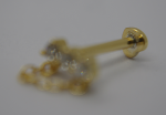 Small gold stud earring with a short chain and butterfly back resting on a white surface, shown soft and out of focus.