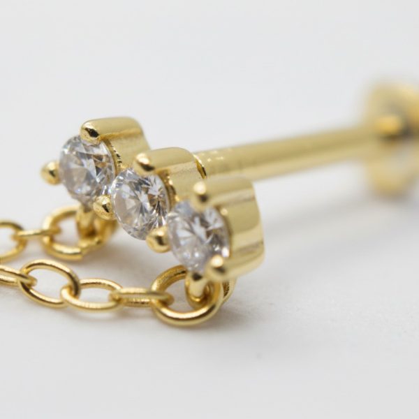 Gold stud earring with three round clear gemstones set in a row, attached to a short delicate gold chain.