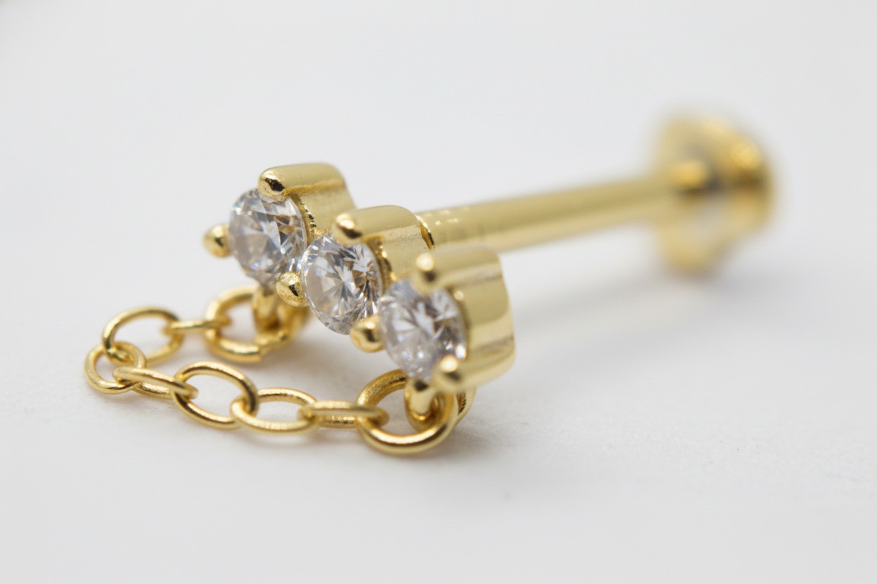 Gold stud earring with three round clear gemstones set in a row, attached to a short delicate gold chain.