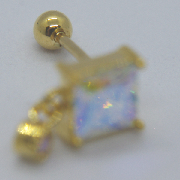 Gold stud earring with a square iridescent gemstone on a white surface, round backing sharply focused while the gem is blurred.