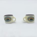 Two small cream mugs with handles on a white background, each showing an oval Central Perk logo and dark brown tops.