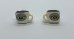 Two miniature cream-colored square coffee mugs with Central Perk logos, filled with dark liquid, on a white surface.