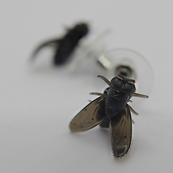 Black fly-shaped stud earring in sharp focus on a white surface with a second matching stud blurred behind