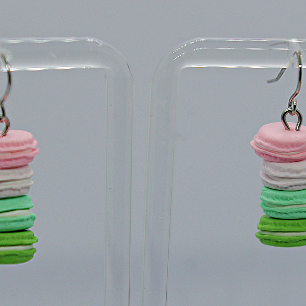 Pair of dangling earrings shaped like stacked pastel macarons — pink, white, mint and green — hanging on a display stand.