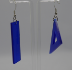 Asymmetric blue acrylic earrings shaped like a small ruler and a triangular set square hanging from a clear earring stand.