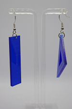 Blue acrylic geometric dangle earrings on clear stand: left ruler-like rectangle, right diamond with triangular cutout.