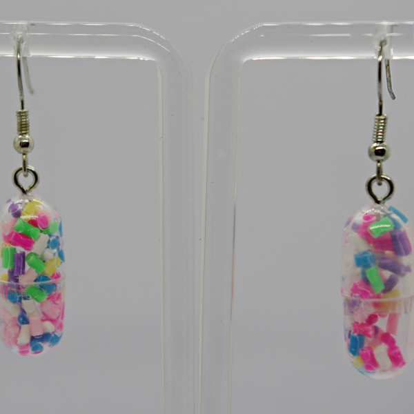 Clear capsule drop earrings filled with colorful pink, green, blue, purple and white confetti beads on a transparent display stand.