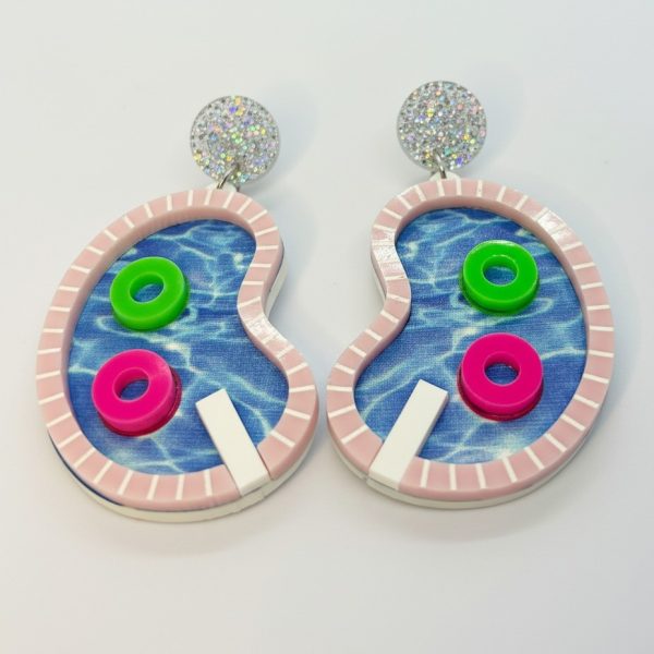 Pair of whimsical pool-shaped dangle earrings with blue water print, pink striped rim, glitter studs, and neon float rings.